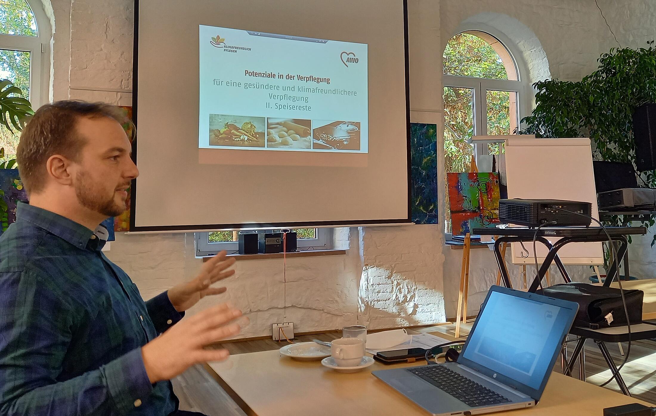 Mensch an einem Tisch vor Leinwand erklärt etwas